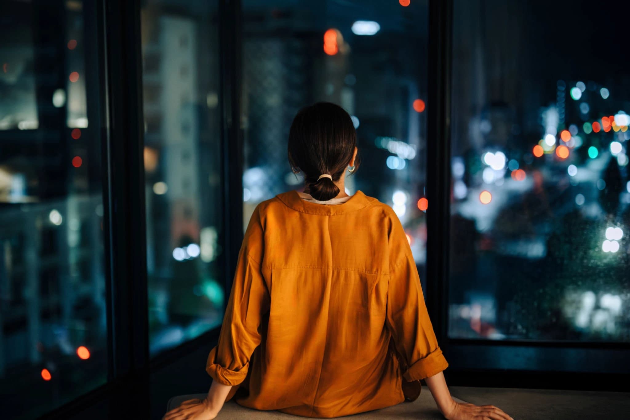 Person in an orange top looking out over a city at night.