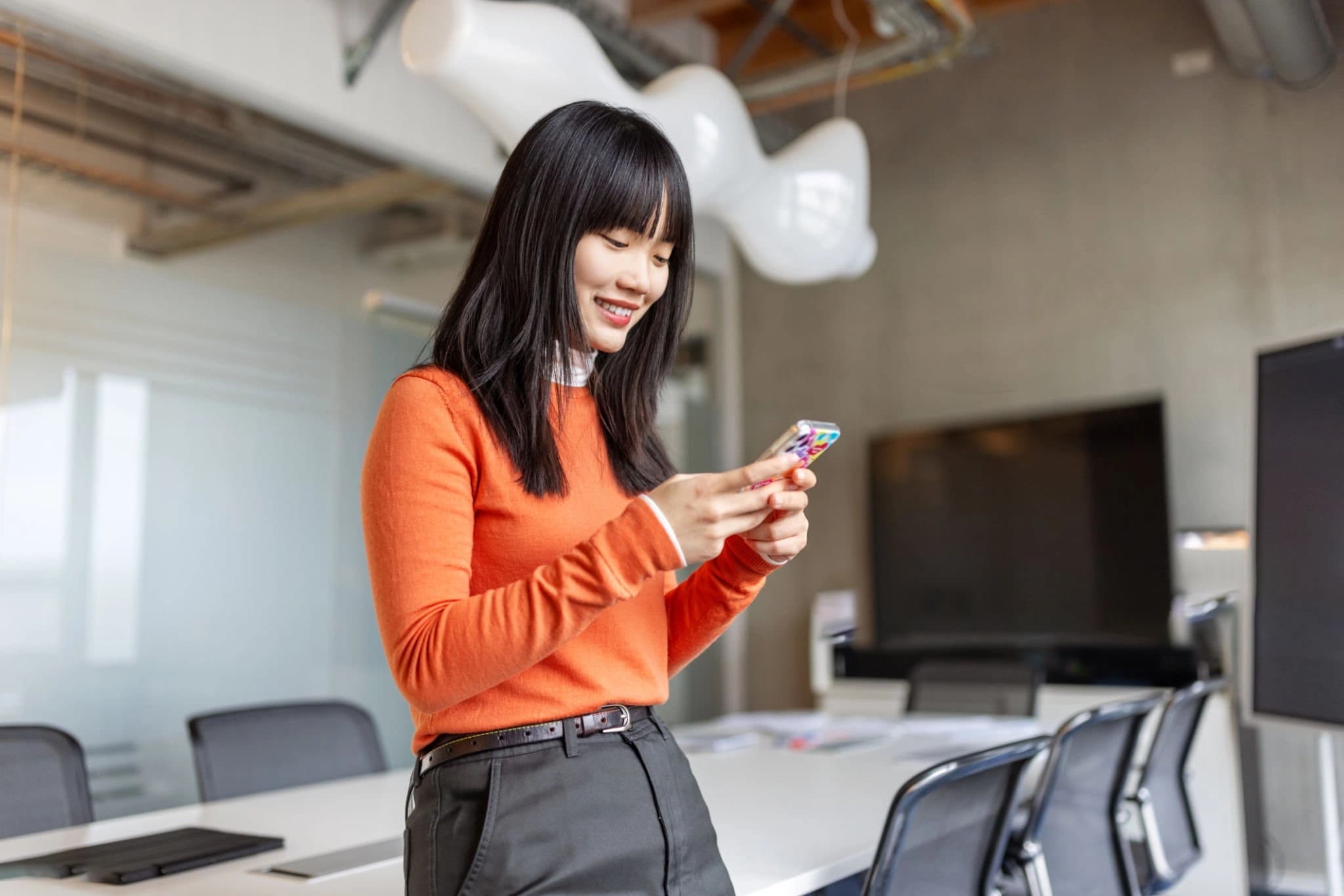 Person in an orange top using a phone in a shared workspace.